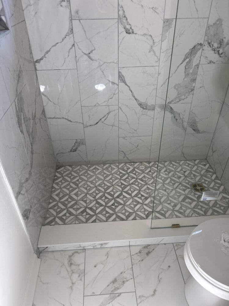 Walk-in shower with large marble-look wall tile and a patterned mosaic floor