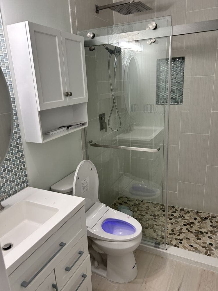 Remodeled bathroom with a glass walk-in shower, pebble shower floor, white vanity and over-toilet cabinet