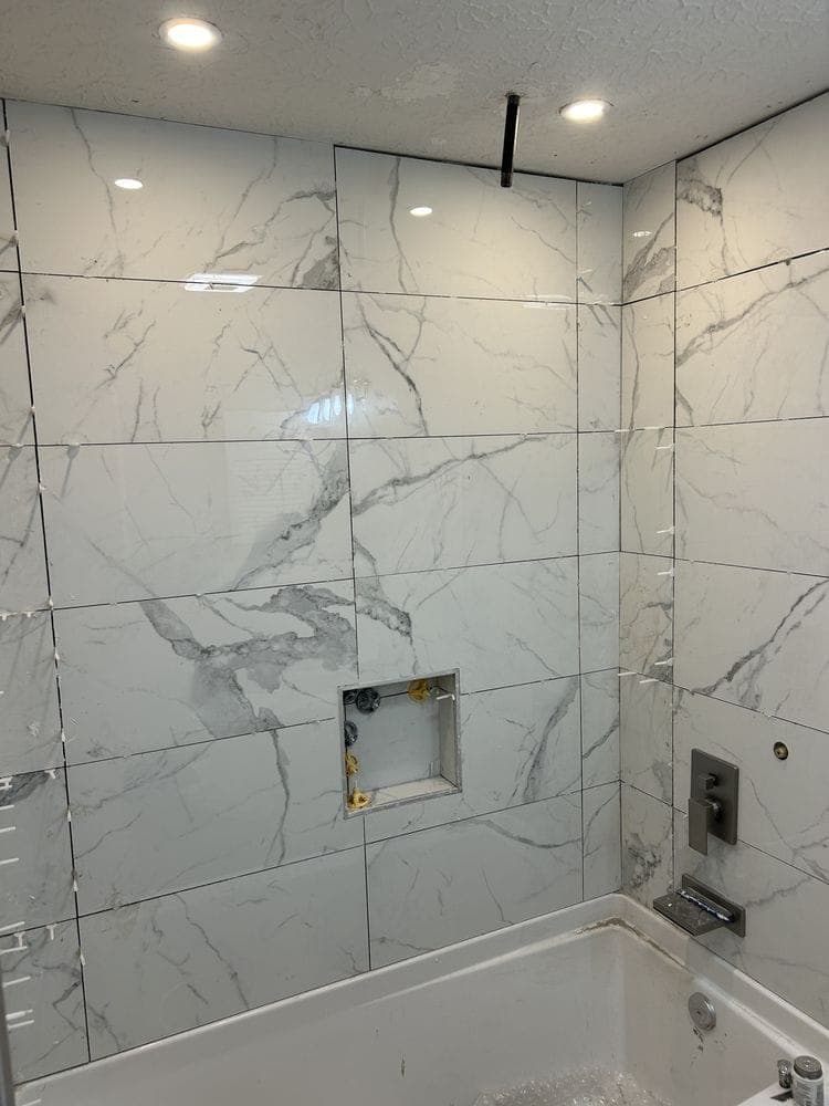 New bathtub with a Carrara marble-look tile surround and a tiled niche