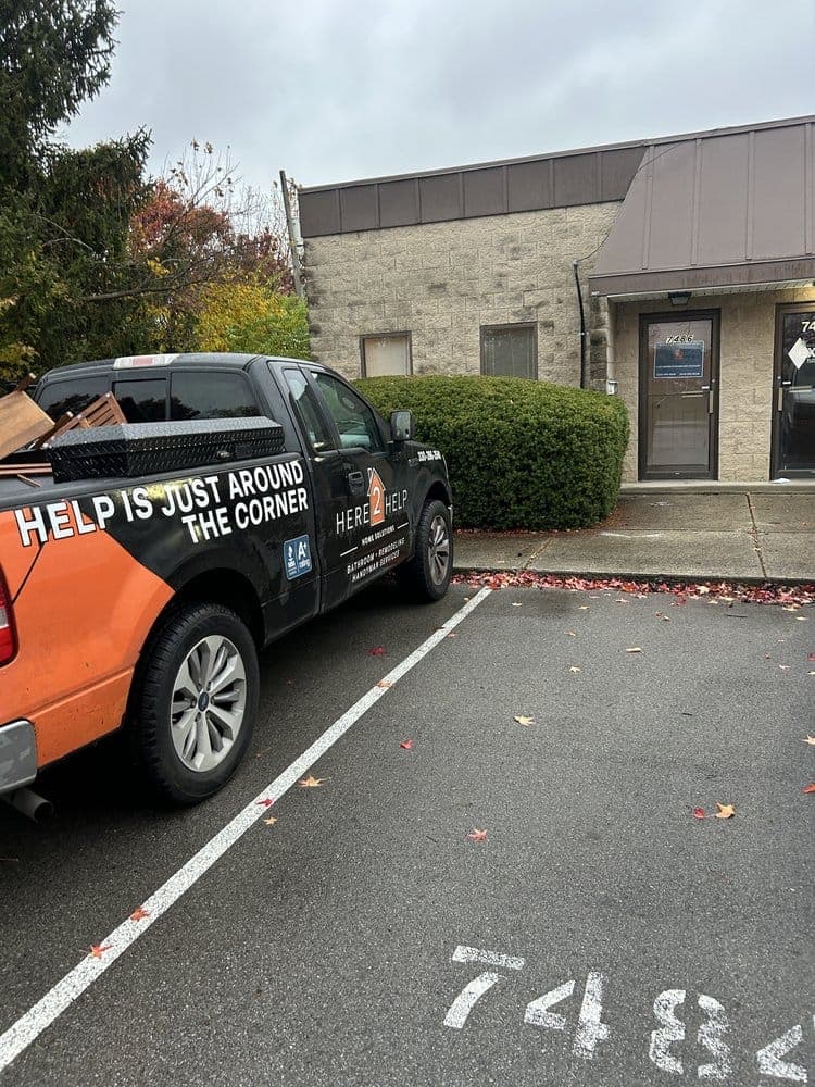 Here 2 Help Home Solutions work truck, wrapped in black and orange, parked outside their showroom