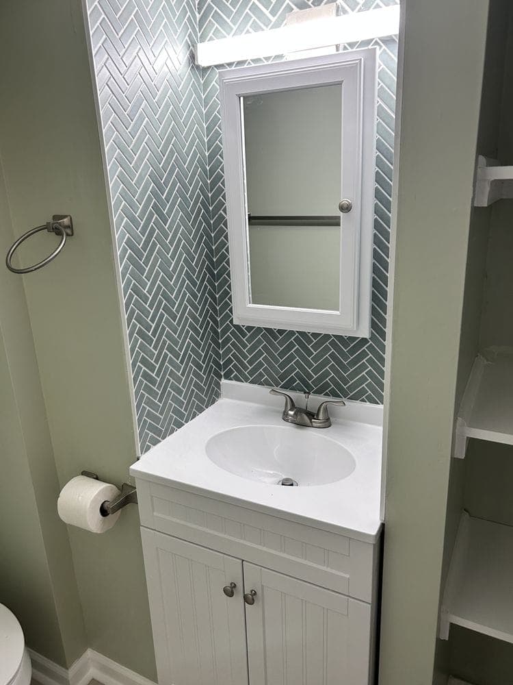 Herringbone glass tile wall behind a white vanity and medicine cabinet