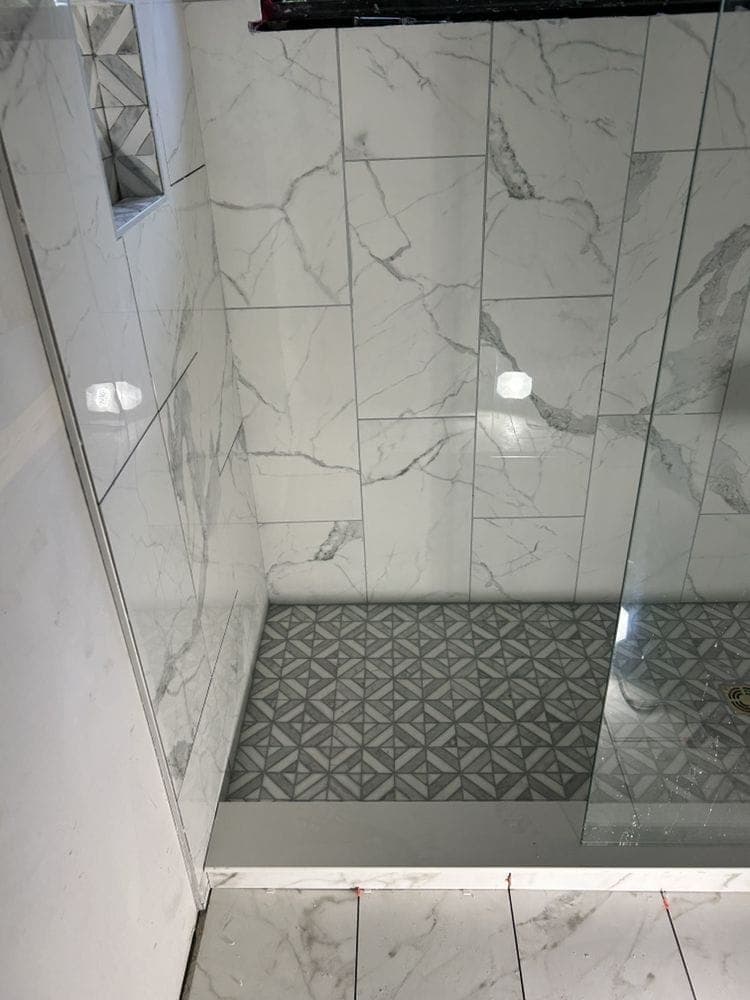 Bath-to-shower conversion in Dublin with marble-look wall tile, a patterned mosaic floor and a glass panel